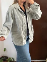 Campera de jean verde claro de corte oversize, con bolsillos frontales con solapa en el pecho y bolsillos aplicados en la parte inferior. Cierre frontal con botones metálicos y cuello camisero.