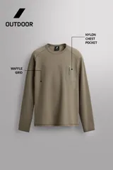 Camiseta relaxed fit de color verde militar, confeccionada en tejido con estructura waffle. Tiene cuello redondo, manga larga con puño elástico y un bolsillo plastrón con cierre de cremallera en el pecho.