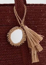 Bolso tote de tejido de fibra natural color bordó, con dos asas largas para hombro y detalle de charm colgante con flecos.