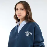 Buzo azul de cuello en V con estampa frontal, que incorpora una camisa de rayas verticales celeste y blanca debajo, creando un efecto de capas.