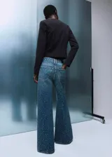 Jeans de tiro medio con diseño wide leg, confeccionados en tejido de algodón estilo tejano. Presentan un acabado con adorno de strass, cierre de botones y cinco bolsillos.