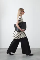 Vestido corto de silueta amplia con corte bajo busto, cuello a la base y mangas cortas. Presenta un estampado de lunares negros sobre fondo beige claro.