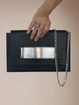 Sobre de cuero negro con aplique horizontal plateado y cadena metálica plateada.