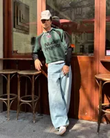 Suéter de punto Nude Project con diseño inspirado en camisetas de fútbol retro. Presenta un patrón de rayas verticales en tonos verde, negro y gris, con el logo de la marca en gran tamaño y una rosa bordada en el pecho. Posee cuello redondo acanalado y mangas largas con puños elásticos.