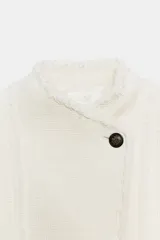 Blazer de cuello alto confeccionada en mezcla de algodón con textura tipo tweed. Presenta un diseño con acabados desflecados, cierre frontal con un solo botón y bajo con detalle peplum.