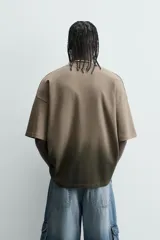 Camiseta de corte relajado (relaxed fit) con cuello redondo y manga corta. Presenta un estampado frontal con relieve en la zona del pecho con el texto "Endless Echo", y un efecto de teñido degradado que va del marrón claro al marrón oscuro/negro en la parte inferior.