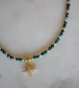 Collar de crisocola con cuentas facetadas en tonos verdes y azules, intercaladas con pequeñas cuentas doradas. Incluye un dije de cruz del norte en baño de oro con incrustaciones de circonias.