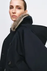Trench corto de corte recto con capucha y cuello desmontable efecto pelo. Presenta cierre frontal con botones, bolsillos laterales y mangas largas con trabillas en los puños.