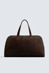 Bolso de viaje de gran tamaño confeccionado en piel con acabado de serraje. Cuenta con un compartimento principal con cierre de cremallera e imanes, interior con bolsillo con cierre y bolsillo plano, y dos asas de mano de piel.