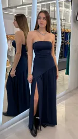 Vestido largo azul marino strapless con escote recto, corte ajustado en el torso y falda larga con tajo lateral profundo y detalle de volados en la parte inferior.