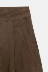 Pantalón de tiro alto con diseño balloon, presenta pliegues frontales, trabillas para cinturón, bolsillos laterales y cierre frontal con cremallera y botón.