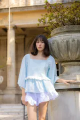 Blusa celeste de tela liviana con escote cuadrado, mangas tres cuartos amplias y detalle de volado horizontal en la parte frontal.