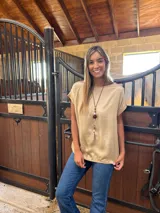 Blusa de satén color beige con cuello redondo, mangas cortas con dobladillo y corte holgado. La parte trasera está confeccionada en algodón con lycra para mayor comodidad y movilidad.