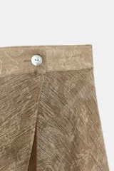 Falda midi de tiro alto y diseño asimétrico con cierre frontal cruzado y botón decorativo. Presenta una textura rústica con estampado sutil y forro interior marrón.