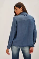 Camisa de denim azul con bordados negros en el frente, de manga larga, cuello clásico y cierre frontal con botones.