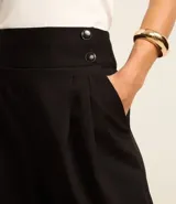 Pantalón zanahoria de sastrería color negro, con cintura alta, pliegues y botones decorativos en los laterales.