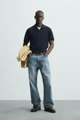 Jersey de punto color verde oliva, de calce relajado (relaxed fit), con cuello solapa y abertura frontal en forma de V. Es de manga corta y presenta acabados en rib en puños y ruedo.