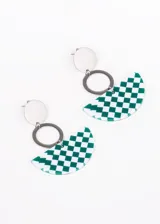 Par de aros colgantes con base de acero quirúrgico, un dije circular plateado, un aro plateado y un dije semicircular de acrílico con estampado a cuadros blancos y negros.