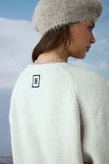Cardigan tejido de punto en color natural, con cuello redondo, cierre frontal de botones oscuros y dos bolsillos delanteros. Presenta mangas largas con puños acanalados.