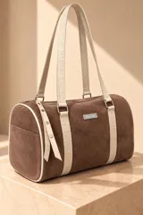 Cartera tipo baulito de cuero color marrón tostado, con doble asa larga de hombro, cierre superior y detalle de placa metálica con el logo de la marca en el centro.