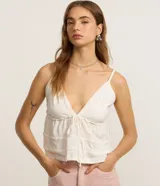 Blusa blanca de algodón y poliéster con breteles finos, escote en V con lazo ajustable y detalles de recortes decorativos.