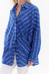 Camisa oversize de algodón con estampado de rayas multicolor en distintas direcciones, cuello camisero, mangas largas y detalle de botonera vertical en la espalda.