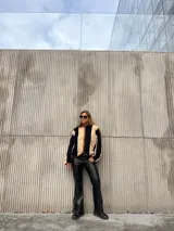 Campera de corderito con diseño de rayas verticales en colores beige y negro, con cierre frontal y detalles de ribete en color marrón.