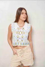 Chaleco de crochet sin mangas, con cuello estilo camisa y cierre frontal de botones. Diseño tejido con patrones geométricos en tonos blanco, celeste y verde oliva.