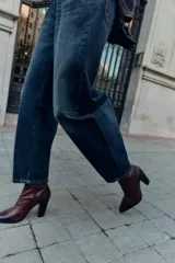 Botín de piel en color bordó con estilo campero. Presenta pespuntes decorativos en la parte frontal y trasera, cierre mediante cremallera lateral y acabado en punta con tacón alto.