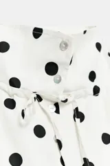 Chaqueta blanca con estampado de lunares negros, cuello subido ajustable con cordón, cierre frontal con botones y bajo ajustable con cordones.