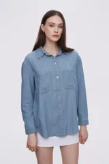 Sobrecamisa celeste de denim con cuello camisero, cierre frontal con botones a presión, dos bolsillos con solapa en el pecho y mangas largas con puños abotonados.