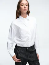 Camisa de algodón de corte clásico con cuello camisero, cierre frontal de botones y canesú en la espalda. Presenta botones decorativos en los laterales que permiten ajustar la silueta.