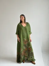 Vestido largo de lino color verde pistacho, con escote en V, mangas tres cuartos y amplio diseño holgado. Presenta un estampado floral grande y artístico en la parte inferior de la falda.
