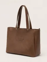 Bolso tipo tote de cuero color marrón, con diseño minimalista, doble asa de mano y cierre superior. Presenta el logo de la marca grabado en un parche central y detalles de remaches metálicos.