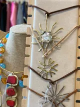 Collar con dije de bronce en forma de sol con incrustaciones de piedras, suspendido de un tiento de gamuza.