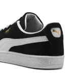 Championes Puma modelo Suede Classic, confeccionados en gamuza negra con la icónica franja lateral en blanco. Presentan cordones blancos, suela de goma texturizada y el logo de la marca en dorado sobre el lateral.