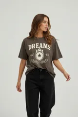 Remera de algodón de corte holgado, con cuello redondo y mangas cortas. Presenta un estampado frontal con la palabra 'DREAMS' y un diseño gráfico tipo escudo con una estrella y detalles florales.