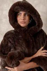 Capa de piel sintética en color negro, con diseño holgado, capucha integrada y bordes con textura de pelo largo.