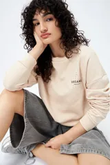 Buzo color beige de algodón con interior suave, corte relajado, cuello redondo y mangas largas. Presenta bordado frontal con la frase "Dreamer - Born to rock" y detalle de estrella con tachas en la espalda.