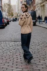 Chaqueta de punto confeccionada en mezcla de lana y alpaca, color beige. Presenta cuello redondo, manga larga, cierre frontal con botones y cinturón ajustable del mismo tejido. Incluye bolsillos delanteros de plastrón y detalles de flores bordadas en color marrón a contraste en la parte superior y en los bolsillos.