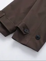 Chaqueta corta de color marrón chocolate, con diseño de doble botonadura, solapas amplias y charreteras en los hombros. Presenta mangas largas con puños ajustables mediante trabillas y bolsillos laterales integrados.
