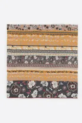 Chal de modal con diseño estampado de bandas horizontales con motivos florales, paisley y geométricos en tonos marrón, mostaza, gris y blanco, con bordes desflecados.