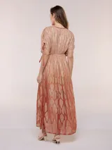 Vestido largo de gasa color salmón con un sutil patrón estampado brillante en tono dorado. Cuenta con escote en V cruzado, cintura imperio elastizada y mangas cortas con tiras ajustables terminadas en borlas.