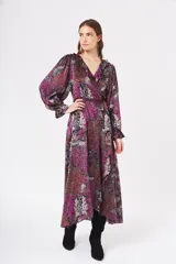 Vestido largo cruzado con estampado floral en tonos fucsia, rojo, blanco y azul sobre fondo negro. Presenta escote en V, cuello con volados y mangas largas abullonadas con puños elásticos. Incluye un lazo para ajustar en la cintura.