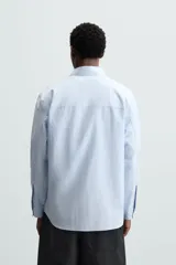 Camisa de manga larga color celeste claro, corte regular fit, con cuello solapa, bolsillo plastrón en el pecho y cierre frontal de botonadura.