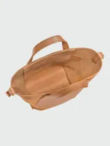 Bolso crossbody Longchamp modelo Complice Softy XS, de cuero tostado, con doble asa superior y correa ajustable para el hombro. Presenta un bolsillo frontal redondo y cierre superior.