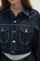 Campera de jean de corte cropped, color azul oscuro con costuras en contraste. Presenta cuello clásico, cierre frontal con botones metálicos y bolsillos frontales con solapa.