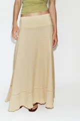 Falda larga de tiro medio en color beige, con tejido de textura cuadriculada. Presenta un diseño acampanado con detalle de costura horizontal y bajo acabado en volante. Cierre lateral con cremallera oculta.