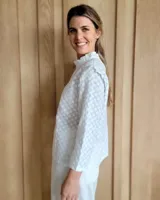 Blusa blanca de manga larga con cuello alto y volados en cuello y hombros.