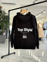 Canguro negro oversize con capucha y gran estampado blanco en la espalda con el texto "Top Style", "Dream big. Work hard. Make it real.", "SINCE 2021" y un código de barras.